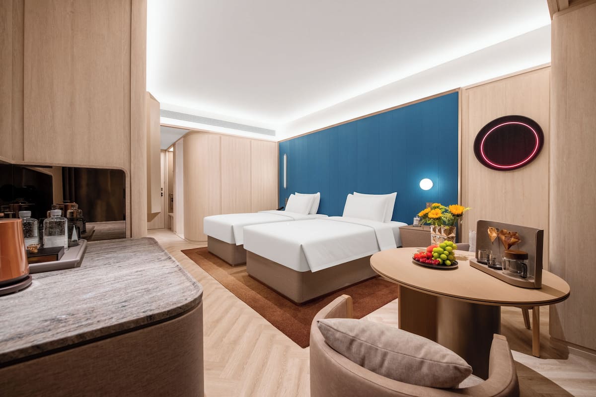 Quarto de hotel moderno com uma cama, uma mesa de escritório e uma pequena mesa com um vaso de flores.