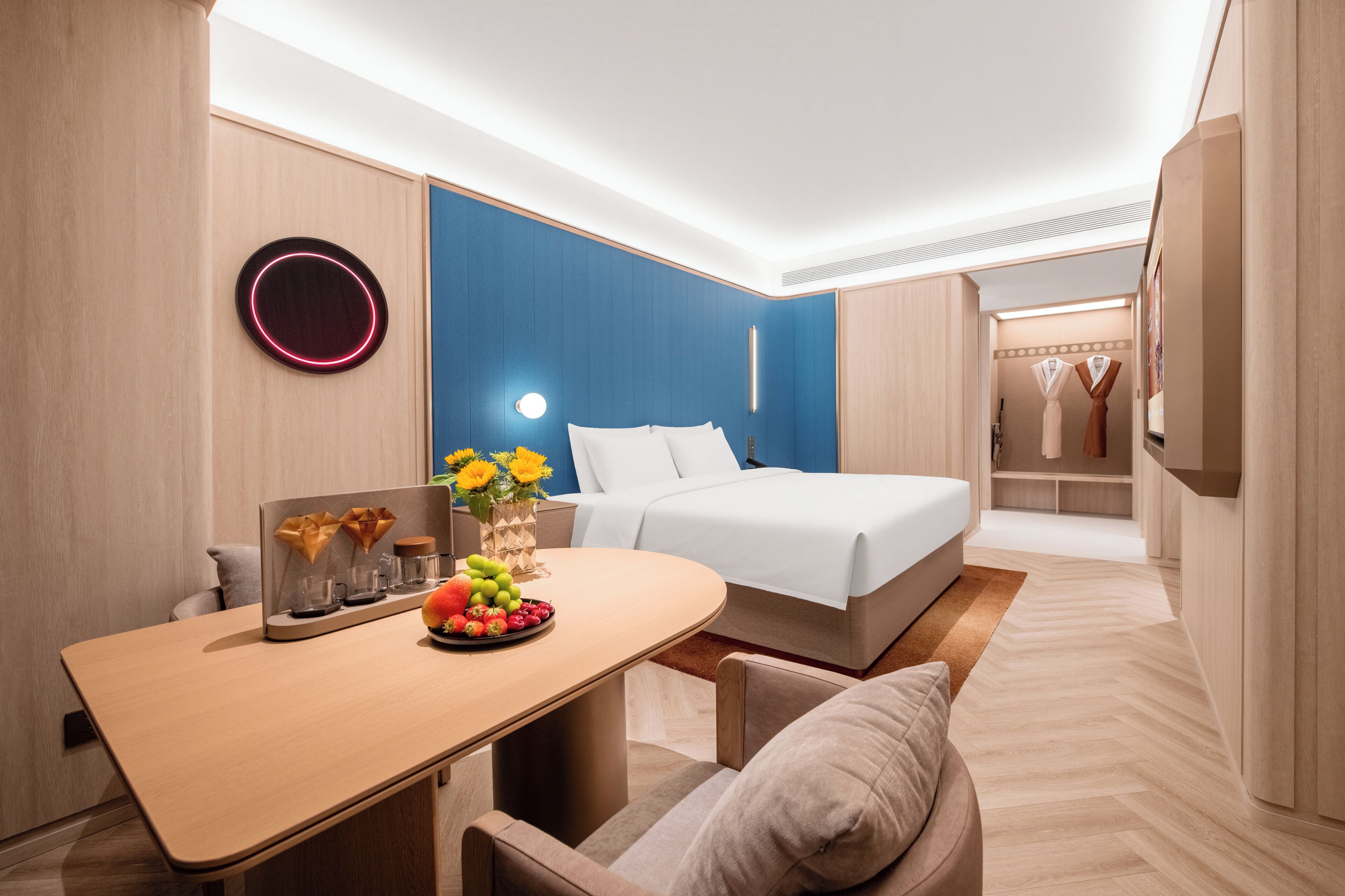 Una habitación de hotel moderna con una cama, un escritorio con frutero, un jarrón con flores y un armario.