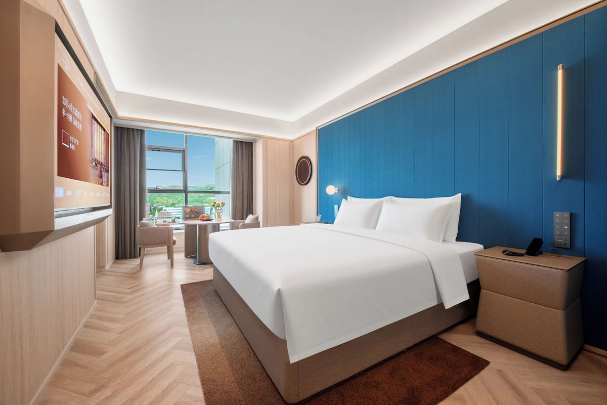 Quarto de hotel moderno com cama grande, mesa de cabeceira e escrivaninha com cadeira.