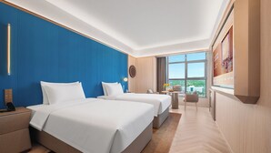 Habitación de hotel con dos camas, una mesita de noche, una pequeña mesa, una silla y un amplio ventanal con vistas.