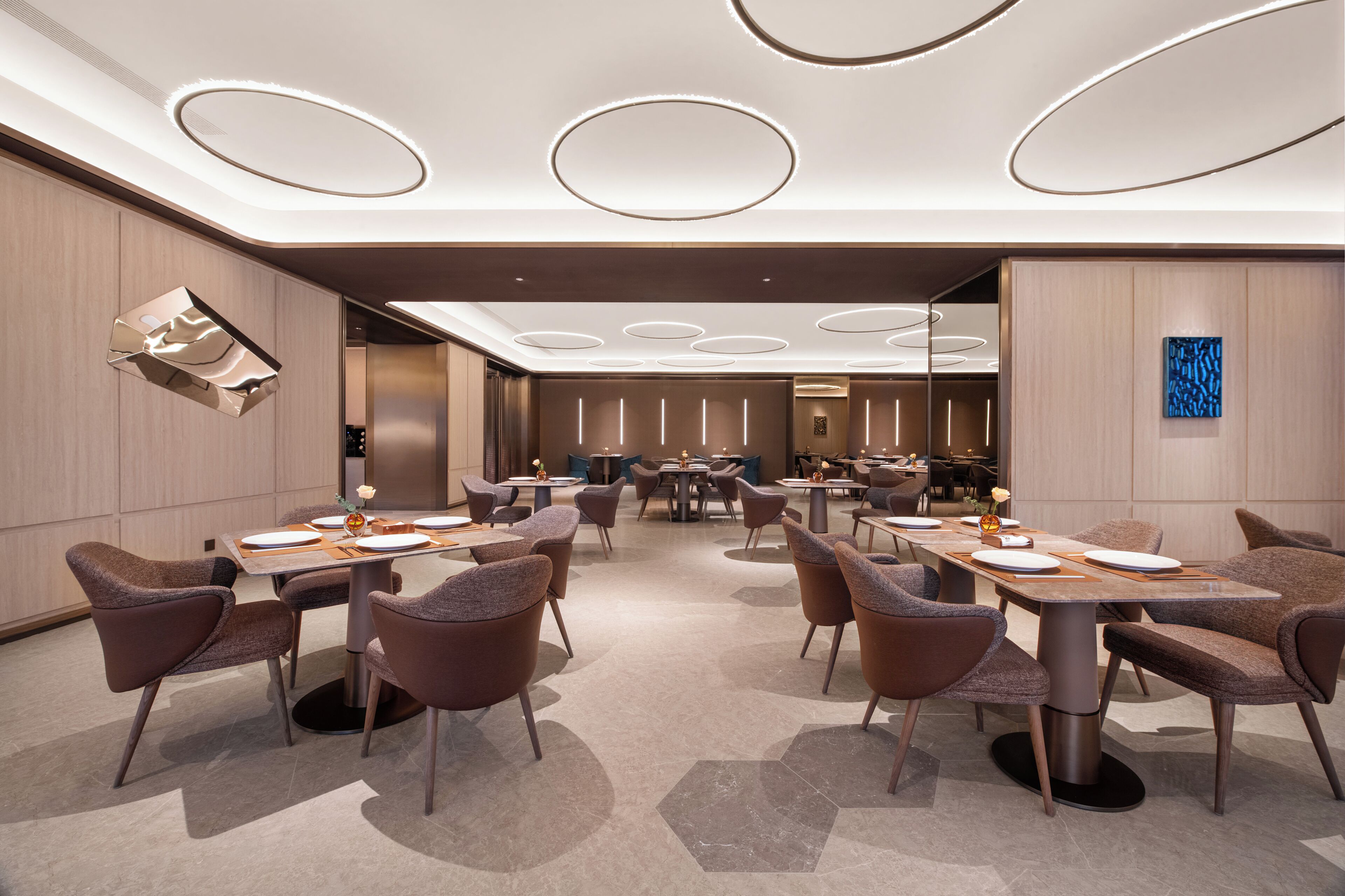 A modern hotel conference room with multiple tables, chairs, and a central area for presentations.