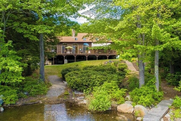 Una cabaña junto al lago con una terraza, un porche cubierto y un estanque natural.