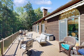 Una terraza de madera con mobiliario exterior, una chimenea de piedra y ventanas grandes.