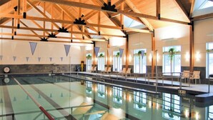 Ein Hallenbad mit Holzbalkendecke, deutlich abgetrennten Bahnen und Liegestühlen.