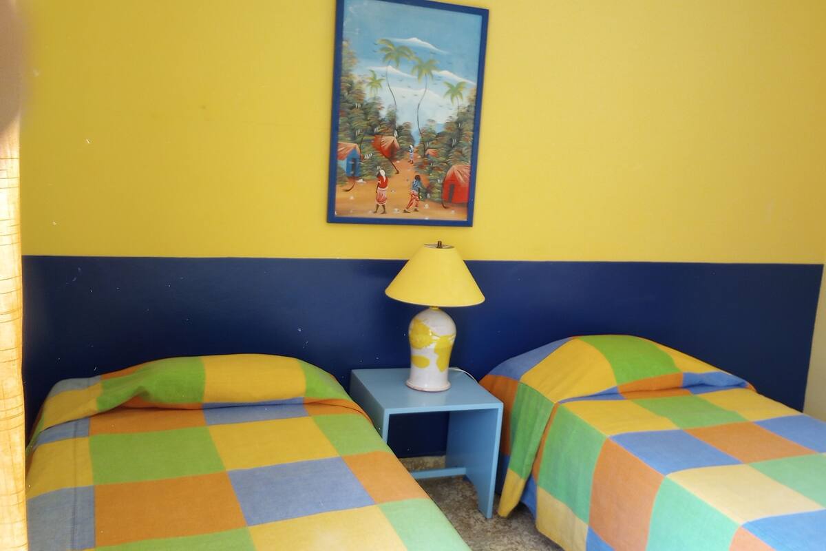 Quarto com duas camas, mesa de cabeceira, abajur e um quadro na parede.