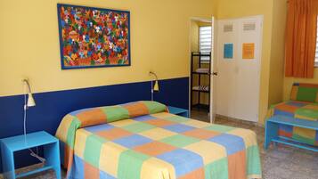 Una habitación con una cama, dos mesitas de noche, una lámpara de pared, un cuadro colorido, un armario y una puerta con avisos.