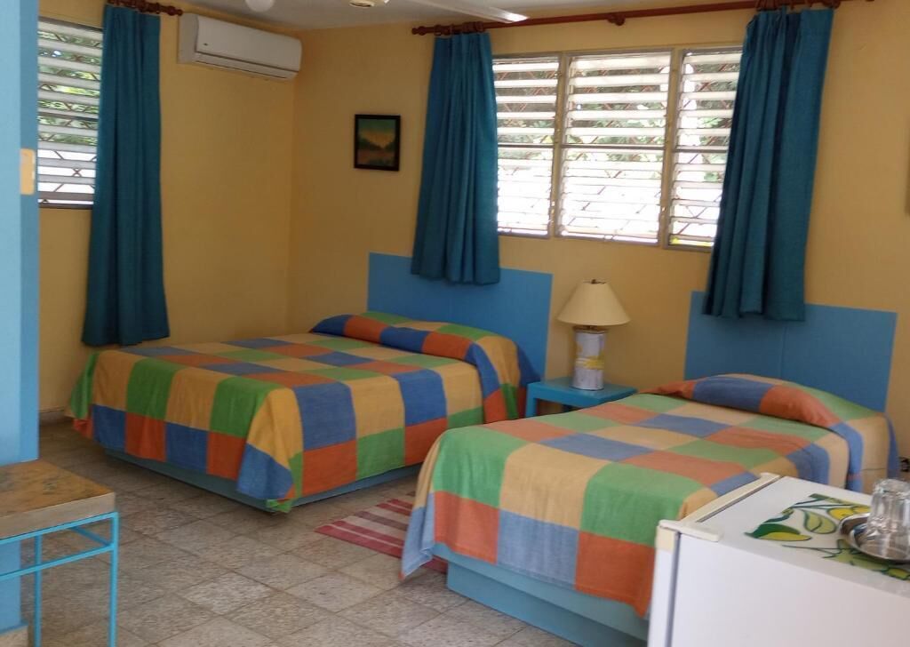 A room with two beds, a small table, a lamp, and a window with curtains.