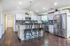 A modern kitchen with white cabinets, stainless steel appliances, and a bar area with stools. - Private Beach Access + Hot Tub / Near Wineries / Lake Erie Retreat / Sleeps 12 (North East)