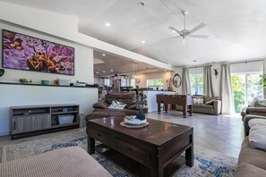 A spacious living room with a large painting, a ceiling fan, and a view into the kitchen. - Private Beach Access + Hot Tub / Near Wineries / Lake Erie Retreat / Sleeps 12 (North East)