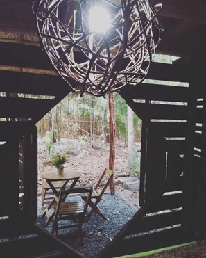 Un área de estar al aire libre con una estructura tejida en el techo, sillas de madera, una mesa y una planta en maceta.