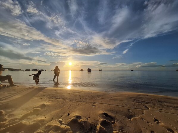 A beach with footprints, a sunset, and boats in the distance.