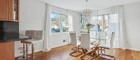 A modern kitchen with a dining area, wooden flooring, and large windows.