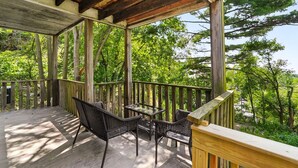 Eine Holzterrasse mit Glastisch und Stühlen, umgeben von Bäumen.