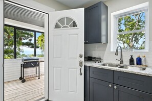 A kitchen with dark cabinets, a white door, a window with a view of trees, and a grill outside. - 6BR · Game Room · Free Parking · Near Stadiums (Pittsburgh)