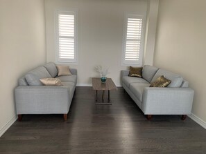 A living room with two grey sofas, a small wooden table, and a vase with white flowers. - Enjoy the comfort of this cozy home, minutes away from downtown! (Kawartha Lakes)