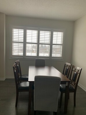 A dining room with a rectangular table, six chairs, and a large window with blinds. - Enjoy the comfort of this cozy home, minutes away from downtown! (Kawartha Lakes)