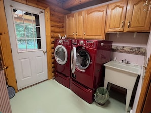 A compact laundry room with wooden cabinets, a washing machine, a dryer, and a sink. - Private Log home in Hiawatha Forest near Pictured Rocks, Munising, waterfalls.! (Munising)