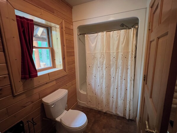 A bathroom with a toilet, a window with a red curtain, and a shower curtain. - Private Log home in Hiawatha Forest near Pictured Rocks, Munising, waterfalls.! (Munising)