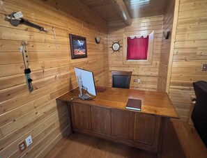 A wooden cabin interior with a desk, a computer, a chair, a window with a red curtain, and a clock on the wall. - Private Log home in Hiawatha Forest near Pictured Rocks, Munising, waterfalls.! (Munising)