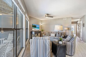A modern living room with a sofa set, a TV, and a ceiling fan. - Direct Beach + Pool Access, Gulf Shores Condo (Gulf Shores)