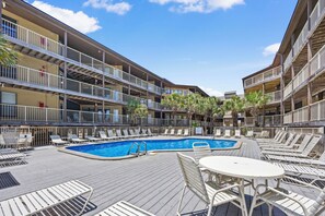 A pool area with lounge chairs and a table, surrounded by multi-story buildings with balconies. - Direct Beach + Pool Access, Gulf Shores Condo (Gulf Shores)