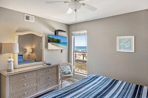 A bedroom with a bed, dresser, chair, ceiling fan, and a window with a beach view. - Direct Beach + Pool Access, Gulf Shores Condo (Gulf Shores)