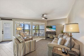 A living room with a sofa, armchairs, a coffee table, a TV, and a ceiling fan. - Direct Beach + Pool Access, Gulf Shores Condo (Gulf Shores)