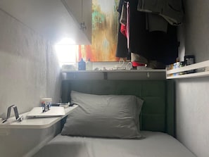 Ein kleiner, kompakter Raum mit einem Etagenbett, einem Nachttisch mit Lampe und einem Fenster mit Außenblick.