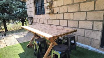 Uma mesa de madeira com bancos, uma parede de tijolos e uma janela com grade de metal.