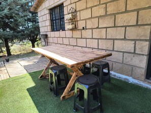Une table en bois avec des tabourets, un mur en briques et une fenêtre avec une grille en métal.