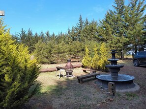 Un jardin agrémenté d’une fontaine en pierre, de bancs en bois et d’un espace barbecue.
