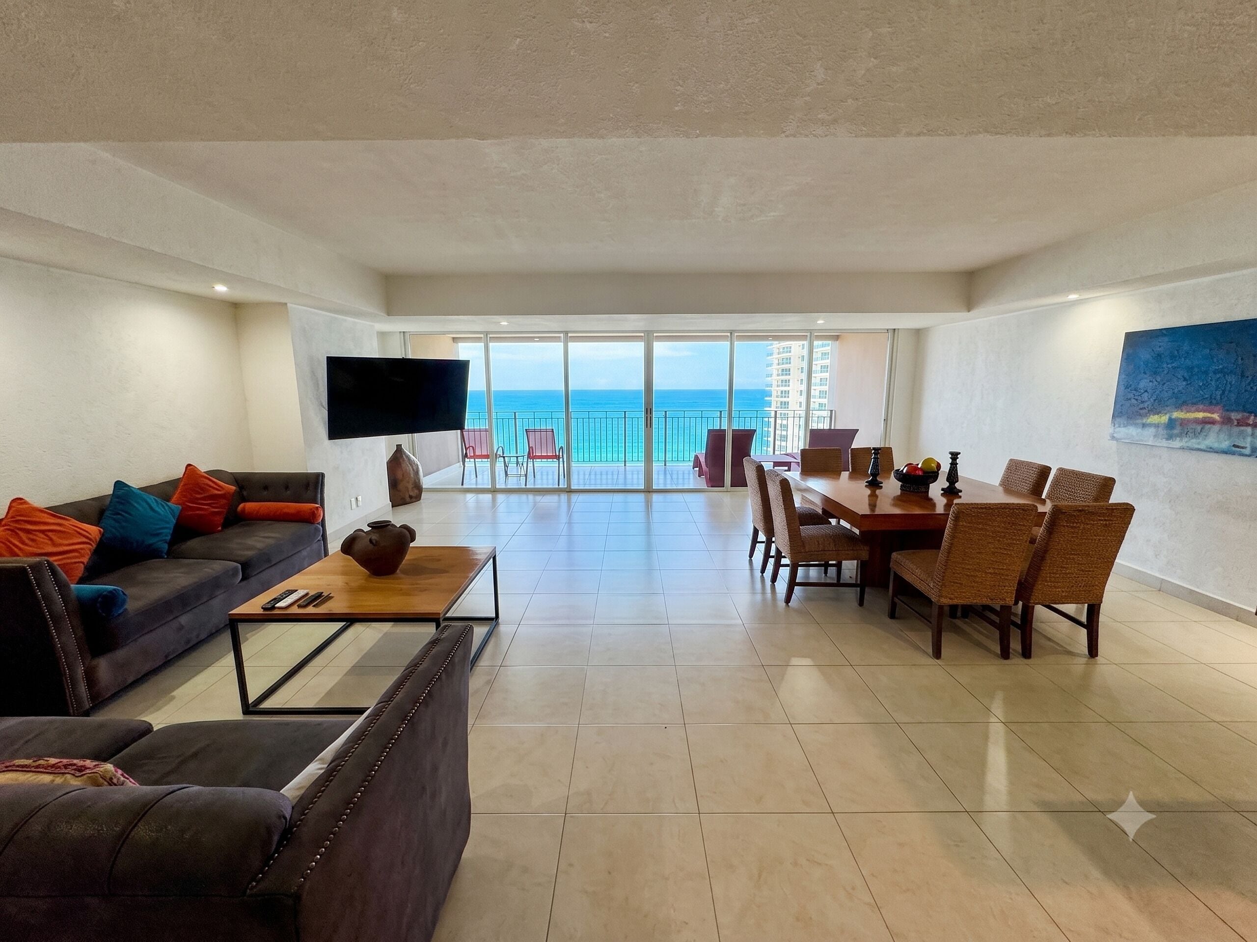 A spacious living area with a sofa, coffee table, TV, dining table, and chairs.