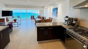 Una cocina amplia con una isla grande, un comedor con sillas y vista al océano a través de ventanas grandes.
