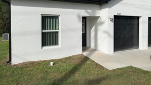 Una casa moderna de un piso con garaje, puerta principal y un pequeño jardín delantero.