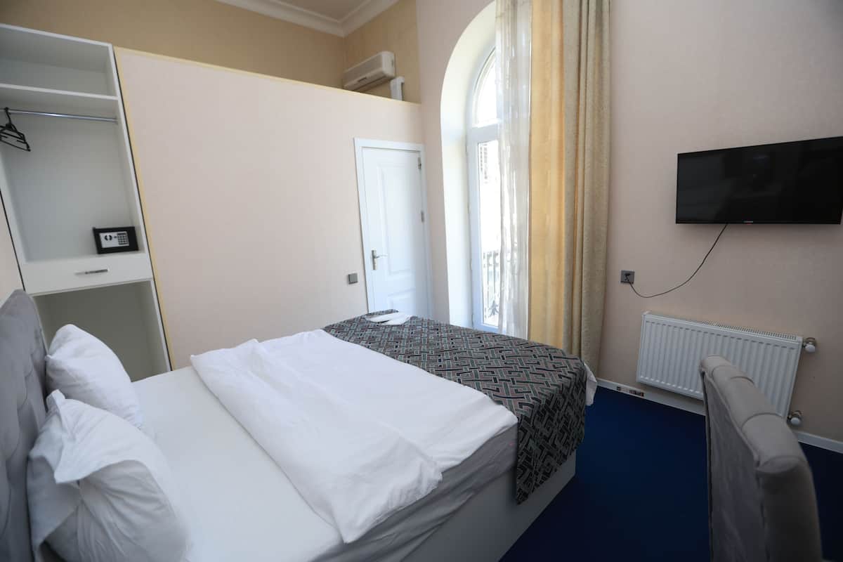 Una habitación de hotel con cama, armario, televisor y ventana con cortinas.