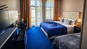 Et hotelværelse med seng, skrivebord, stol, garderobeskab og et vindue med gardiner.