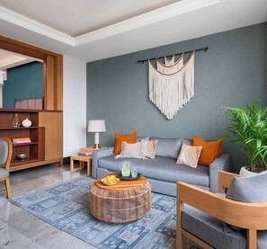 Ein modernes Wohnzimmer mit grauem Sofa, einem Holznachttisch und einem runden Kaffeetisch aus Weidengeflecht.