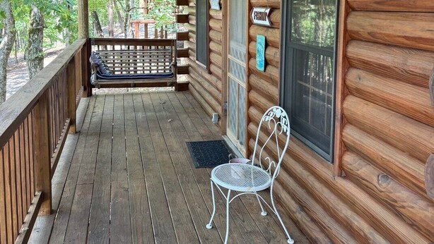A wooden cabin with a porch, a bench, a chair, and a window with a sign. - The Willows on Table Rock Lake, 1 Bed / 1 Bath Log Cabin, Pool, Hot Tub & Dock (Shell Knob)