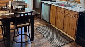 A wooden cabin interior with a kitchen, dining area, and a view of the outdoors. - The Willows on Table Rock Lake, 1 Bed / 1 Bath Log Cabin, Pool, Hot Tub & Dock (Shell Knob)