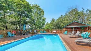 A rectangular swimming pool with a wooden deck surrounding it, equipped with lounge chairs and a small cabin in the background. - The Willows on Table Rock Lake, 1 Bed / 1 Bath Log Cabin, Pool, Hot Tub & Dock (Shell Knob)