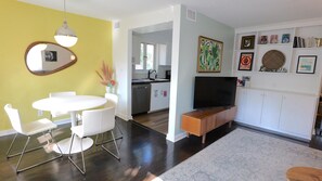 Un salon moderne avec un coin repas, une cuisine à l’arrière-plan et un téléviseur posé sur un meuble en bois.