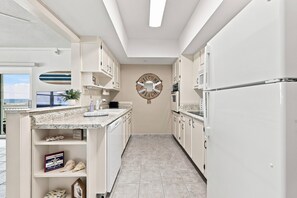 A modern kitchen with white cabinetry, a central island, and a view of the beach through a window.