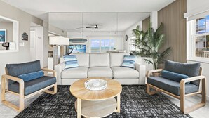 Una sala de estar moderna con un sofá, dos sillones, una mesa de centro y vistas al océano a través de amplios ventanales.