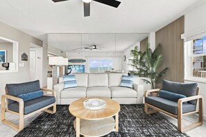 A modern living room with a sofa, two armchairs, a coffee table, and a view of the ocean through large windows.