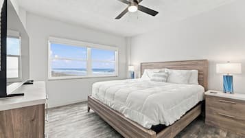 Ein Schlafzimmer mit einem Bett, einem Deckenventilator, einem Fenster mit Meerblick und einem Schreibtisch mit Lampe.