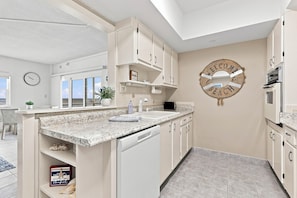 A modern kitchen with white cabinetry, a granite countertop, and a 'WELCOME TO THE BEACH' sign.