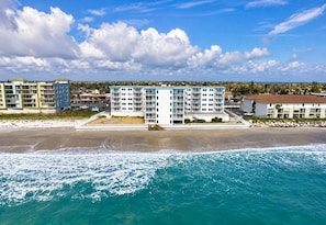 A beachfront hotel with multiple floors, a sandy beach in front, and a view of the ocean.