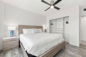 Un dormitorio con cama, mesitas de noche, ventilador de techo, armario y una cesta para la ropa colgada.