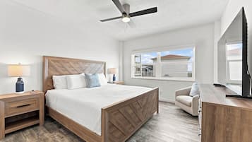 Un dormitorio con cama, mesitas de noche, escritorio, silla, ventilador de techo y ventana con vistas.