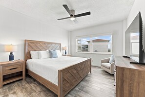 A bedroom with a bed, nightstands, a desk, a chair, a ceiling fan, and a window with a view.